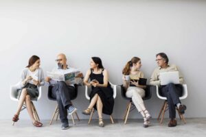 5 Menschen sitzen auf Stühlen, es gibt 2 Gruppen, sie unterhalten sich miteinander.