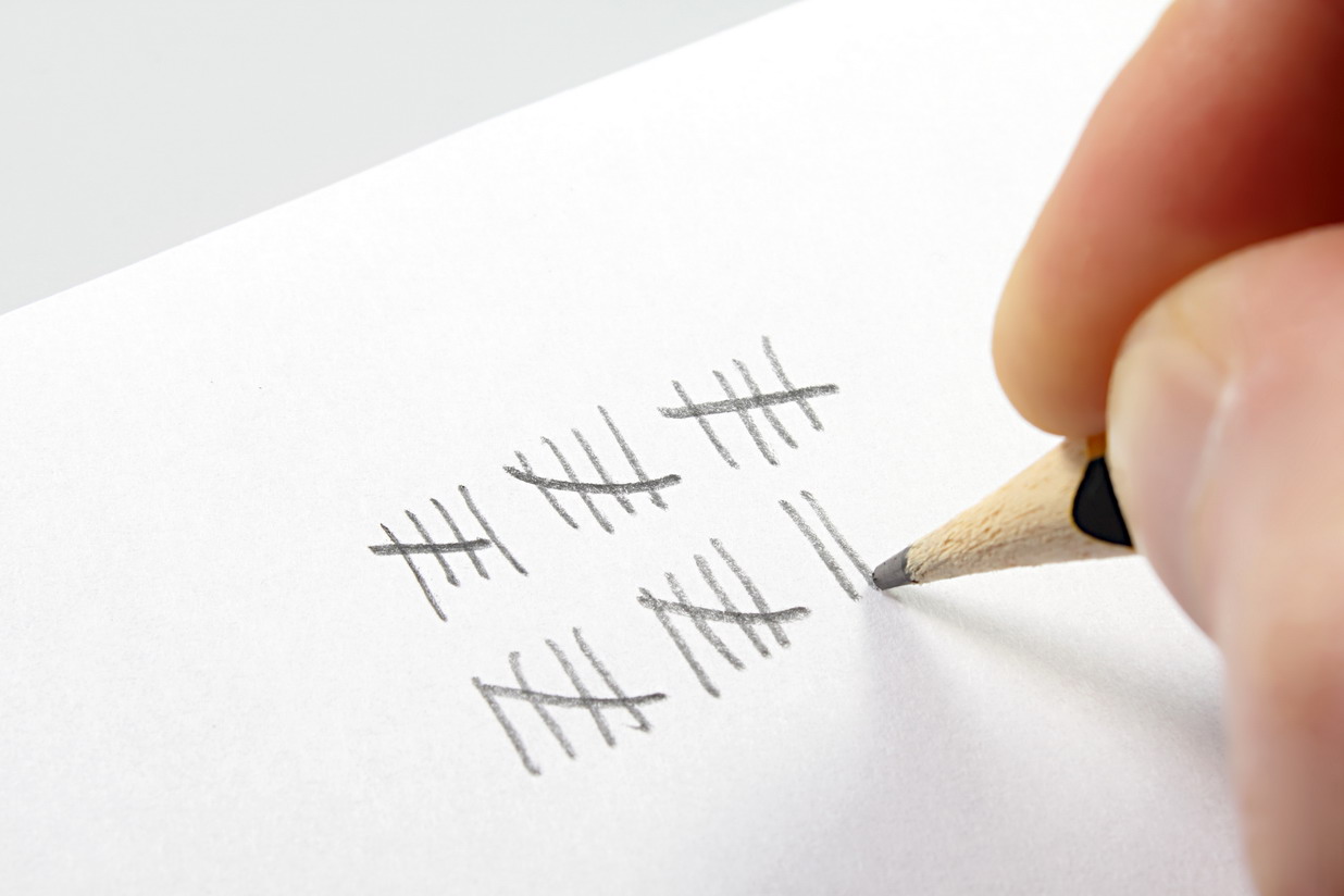 Ein Bleistift hat 5 mal 5 Striche gezeichnet wobei der fünfte Strich die anderen vier Striche durchgestrichen hat. Aktuell ist er bei weiteren 2 Strichen.
