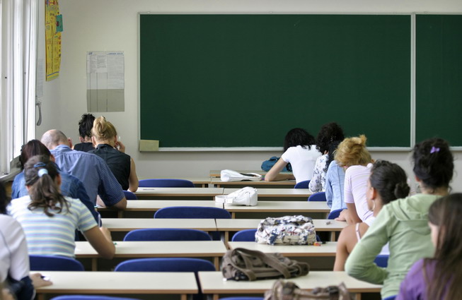 Schüler und Schülerinnen sitzen in der Klasse und schreiben vermutlich eine Klassenarbeit. Sie sind von hinten zu sehen.